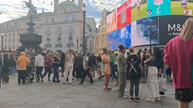 Bustling scene at Piccadilly Circus showcasing diverse crowd and advertising screens.