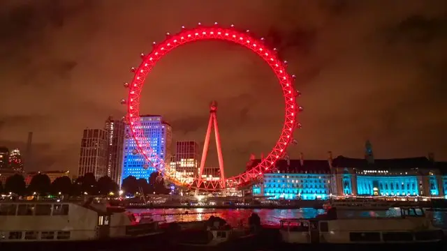 View of the London Eye lit up in colors on a night by the Thames.