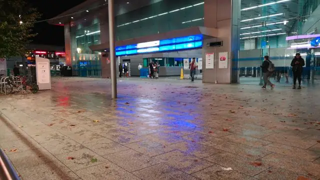 Wet pavement outside a modern railway station at night.