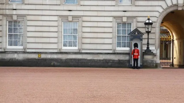 A stoic British guard stands outside Buckingham Palace in traditional attire.