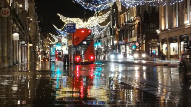 Night shot of a rainy London street with buses, taxis, and festive lights.