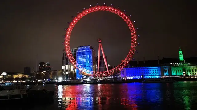 The illuminated London Eye with city lights reflecting on the Thames at night.