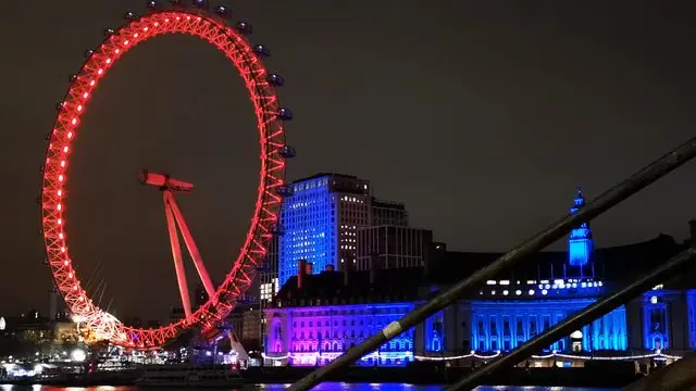 Night view of London Eye illuminated in colors beside the Thames.