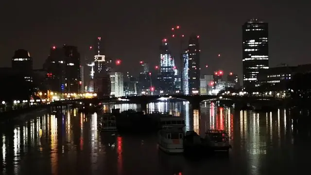 Explore the London skyline at night reflecting on the Thames.