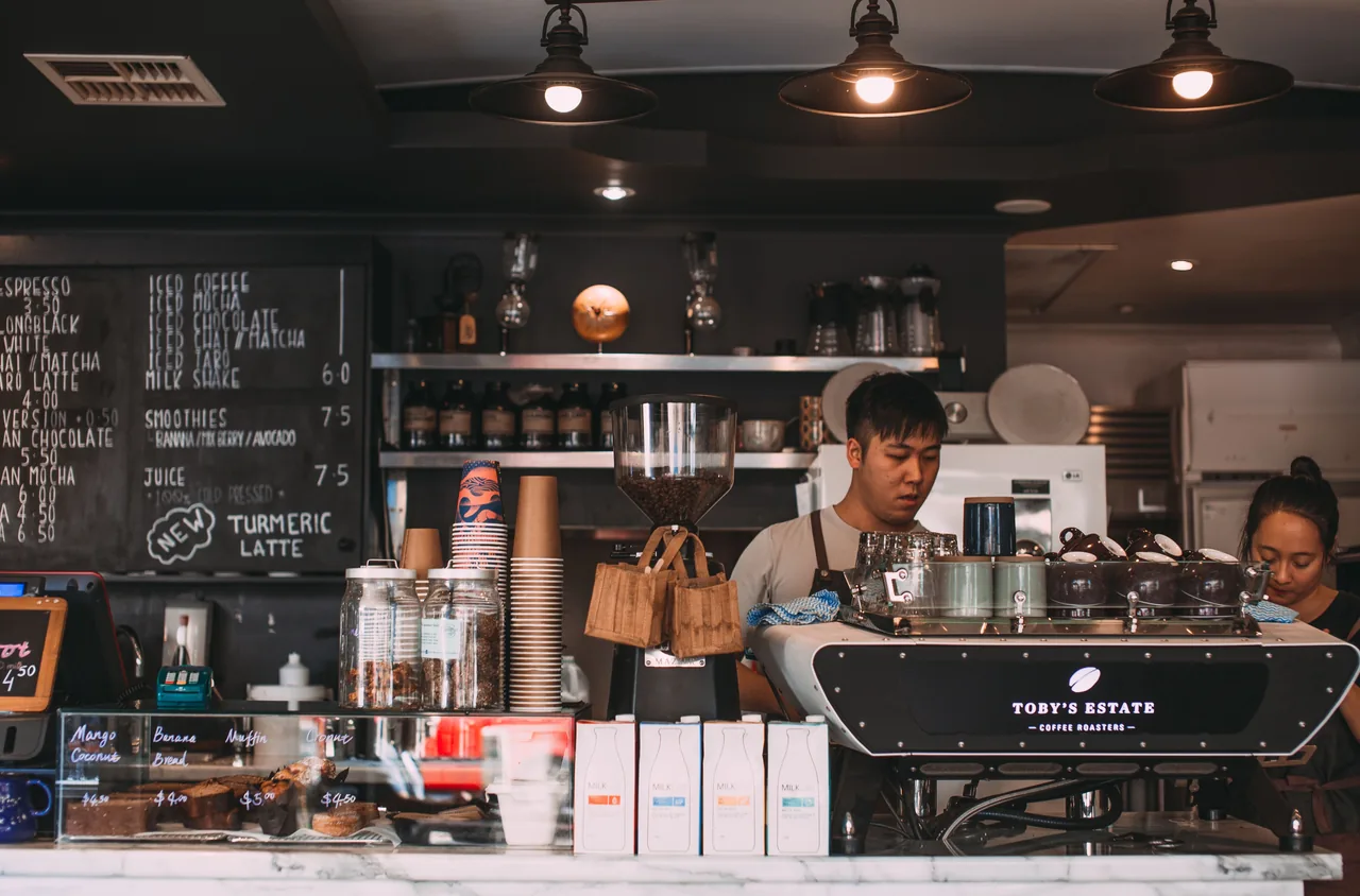 Baristas prepare coffee in a cozy café with a rustic interior design, offering a lively atmosphere.
