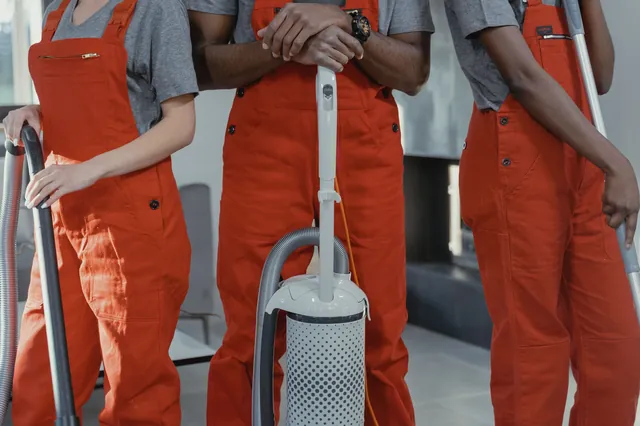 Three cleaning workers in red coveralls with cleaning tools
