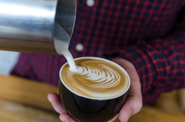 A barista pouring latte art into a cup of coffee