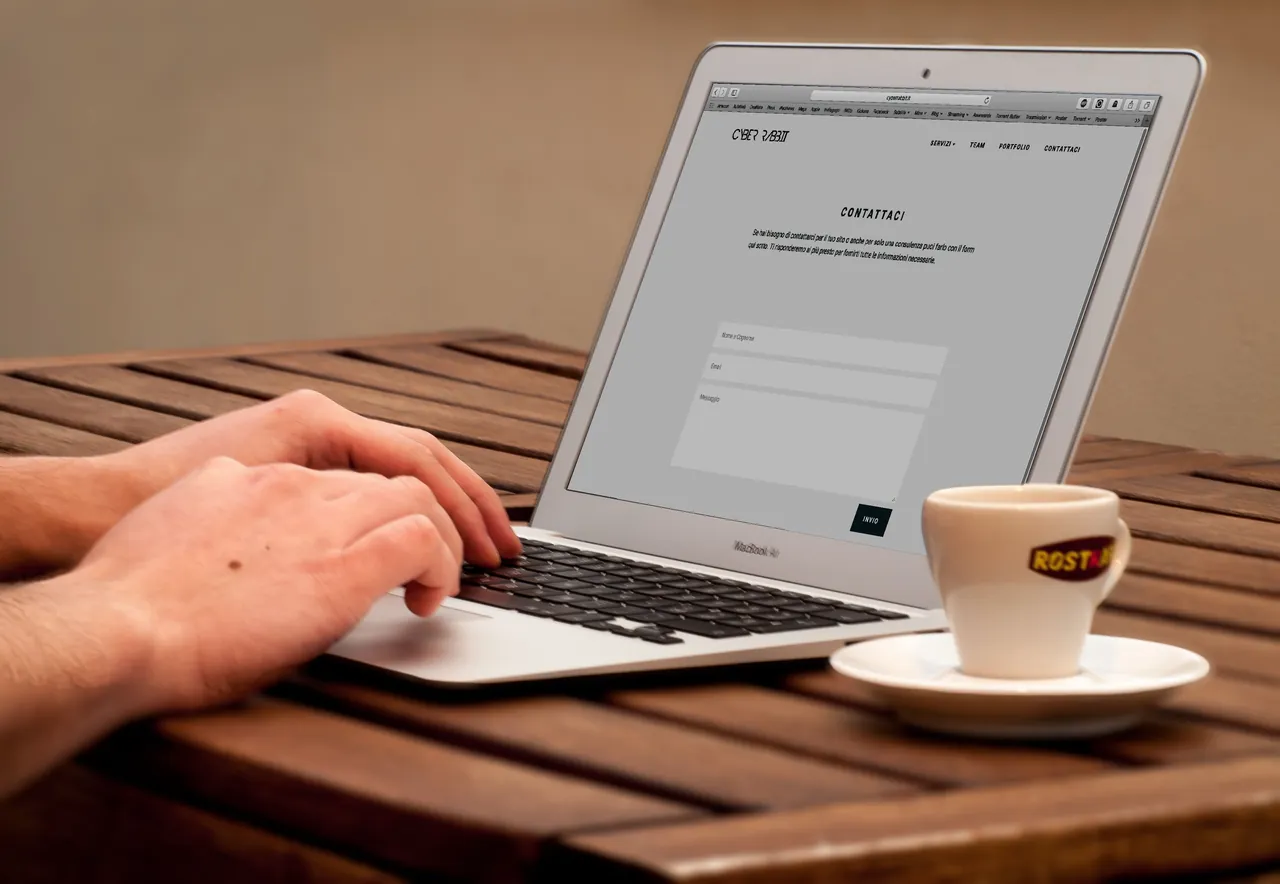 Hands typing on a laptop beside a cup of coffee on a wooden desk